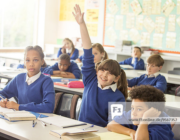 Grundschulkinder im Klassenzimmer während des Unterrichts  lächelndes Mädchen mit erhobener Hand