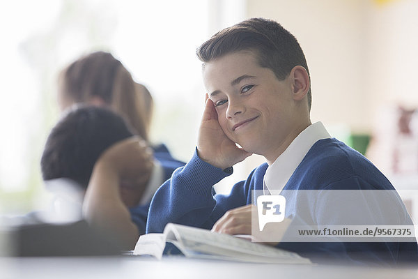 Porträt eines lächelnden Grundschülers am Schreibtisch im Klassenzimmer