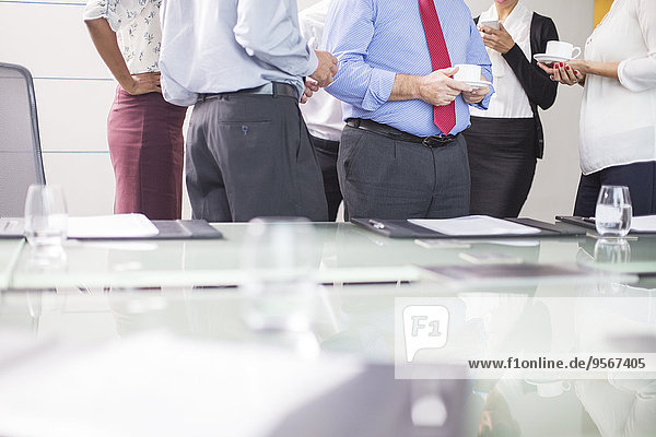 Business people standing in conference room with coffee cups in hands