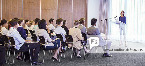 Young woman delivering speech before audience in conference room