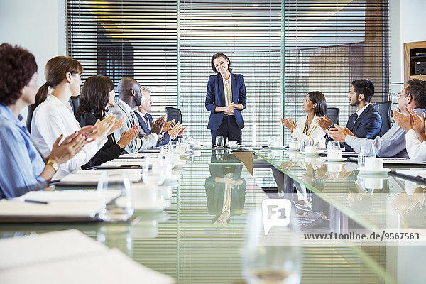 Conference participants applauding to young businesswoman standing at head of conference table