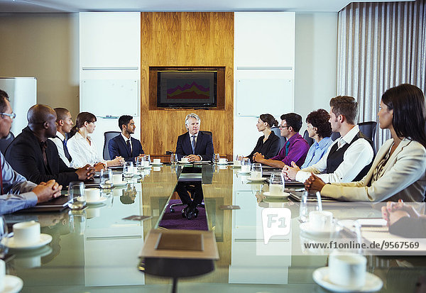 Conference participants looking at man sitting at head of conference table