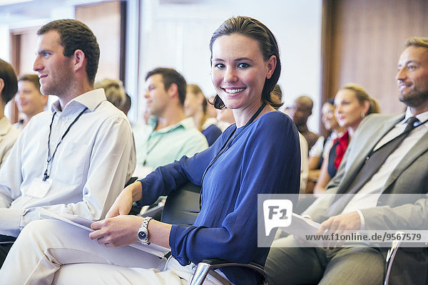 Portrait of smiling young woman sitting in audience in conference room