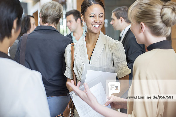 Portrait of two smiling women holding files and talking  standing in crowded lobby