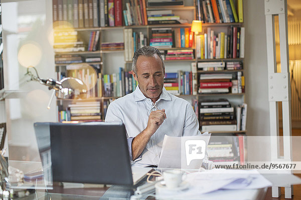 Geschäftsmann beim Lesen von Papierkram am Schreibtisch zu Hause