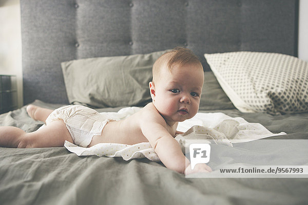 Porträt des kleinen Babys auf dem Bett liegend mit erhobenem Kopf