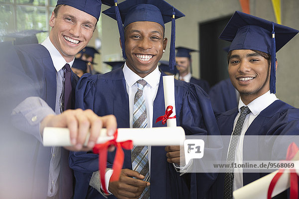 Portrait of smiling university students holding diplomas after graduation ceremony