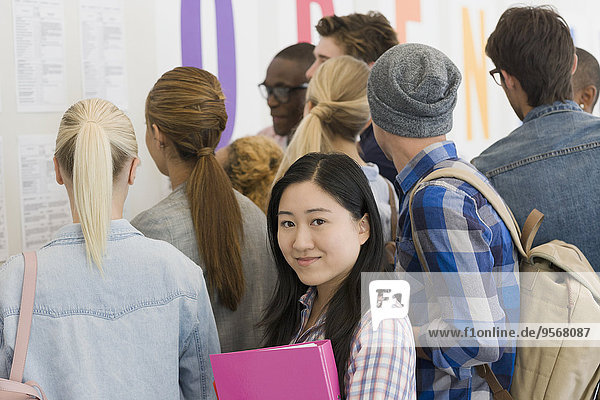 Porträt eines lächelnden Studenten im Flur  Menschen im Hintergrund beim Betrachten der Prüfungsergebnisse