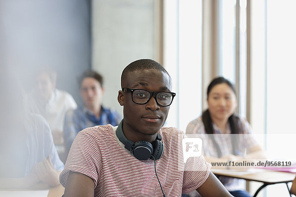Männlicher Student mit Brille und Kopfhörer um den Hals  der während der Vorlesung auf die Kamera schaut.