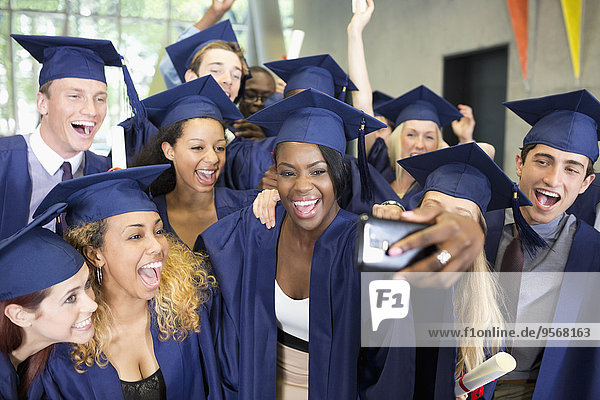 Group of smiling students in graduation gowns taking selfie on graduation day