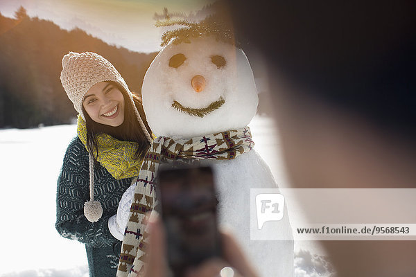 Man photographing woman with snowman