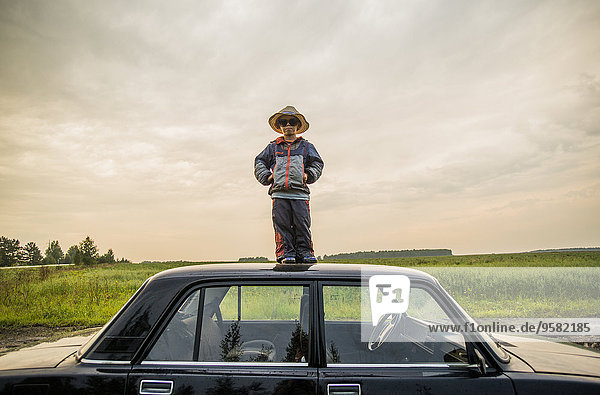 Caucasian boy standing on car roof in rural field