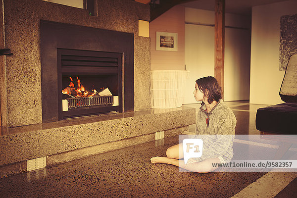Mixed race girl relaxing by fireplace in living room