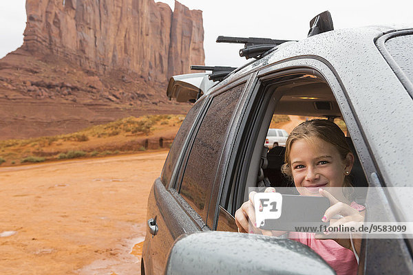 Caucasian girl taking cell phone photograph from car  Monument Valley  Utah  United States