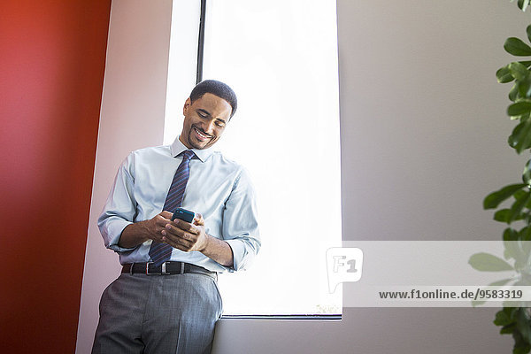 Black businessman using cell phone at office window