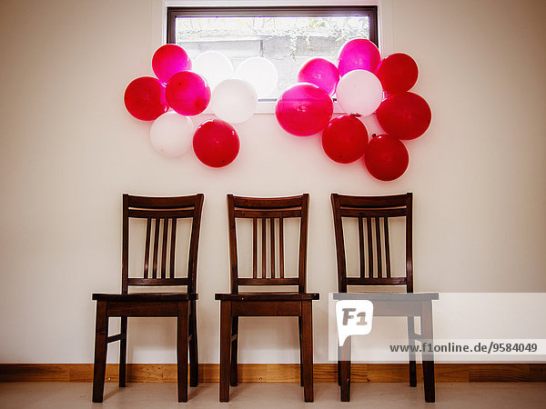 Bunches of colorful balloons over chairs near wall