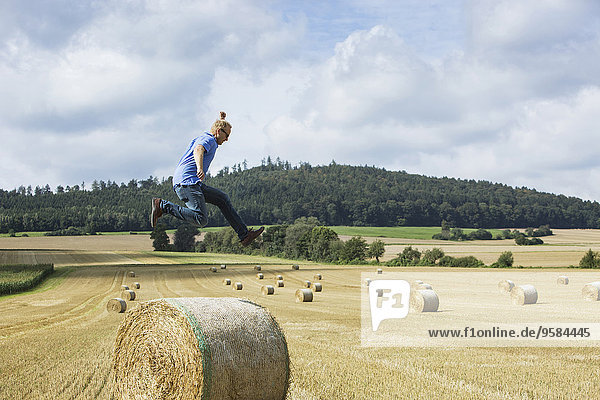 Farmer jumping over hay bale in field
