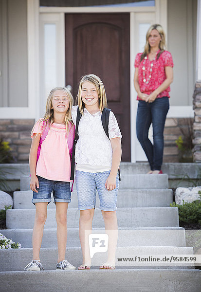 Caucasian sisters smiling on front steps on way to school