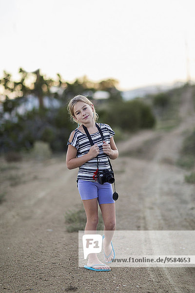 Caucasian girl carrying camera on rural dirt road
