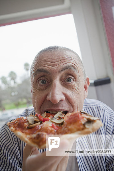 Hispanic senior man eating slice of pizza