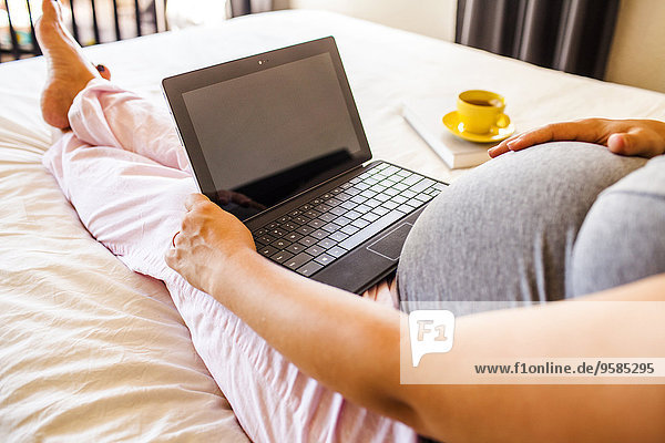 Pregnant Caucasian woman using laptop in bed
