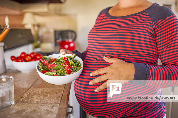 Pregnant Caucasian mother holding salad in kitchen