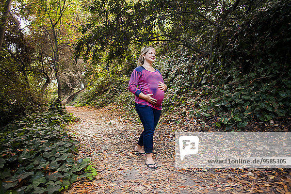 Pregnant Caucasian woman holding her stomach on forest path