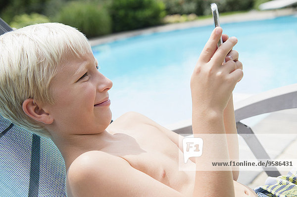 Caucasian boy using cell phone near swimming pool