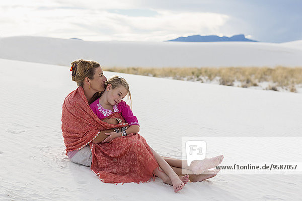 Caucasian mother and daughter wrapped in blanket on sand dune