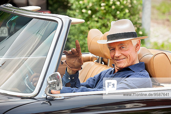 Portrait of a smiling senior sitting in a convertible car waving