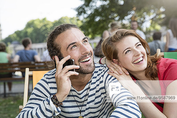 Deutschland  Berlin  Junges Paar im Park  mit Smartphone