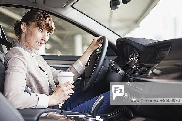 Germany  Hesse  Frankfurt  portrait of smiling businesswoman driving car with coffee to go in one hand