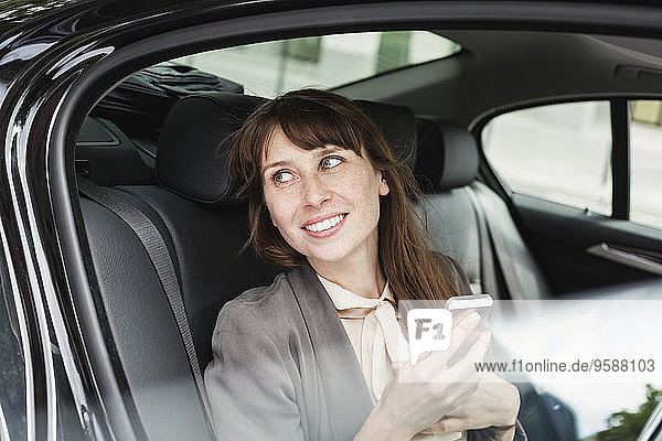 Deutschland  Porträt einer lächelnden Geschäftsfrau im Auto mit Smartphone
