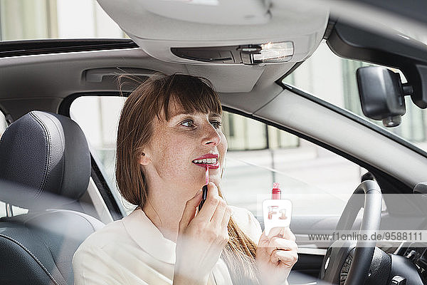 Portrait of businesswoman sitting in her car applying lipstick