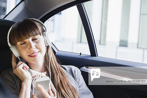 Porträt einer lächelnden Geschäftsfrau mit Kopfhörer  die im Auto Musik hört.