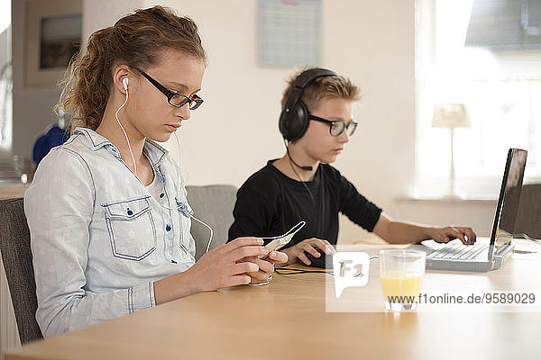 Brother and sister with headphones and earphones using laptop and smartphone