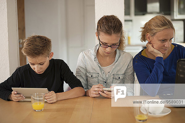 Mother and her two children relaxing with digital tablet  smartphone and laptop at home