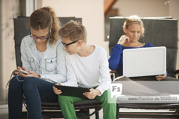 Mother and her two children relaxing with digital tablet  smartphone and laptop on the terrace