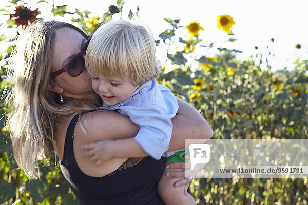 Mid adult woman and toddler hugging in sunflower field
