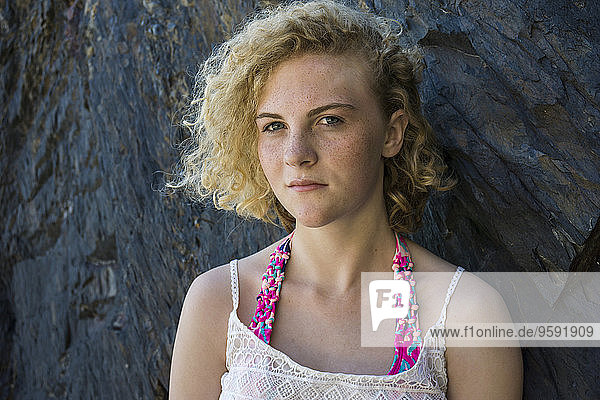 Portrait of teenage girl with freckles standing in front of a rock