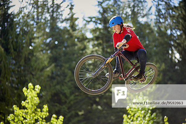 Young female bmx biker jumping mid air in forest