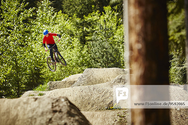 Junge Bikerin  die in der Luft von Felsen im Wald springt.