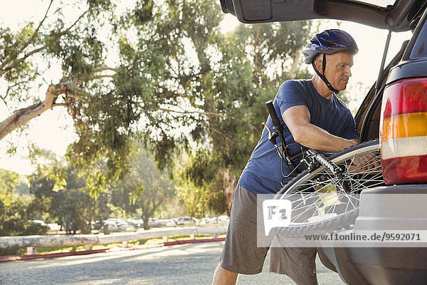 Erwachsener Mann  der das Fahrrad aus dem Kofferraum im Park herausnimmt