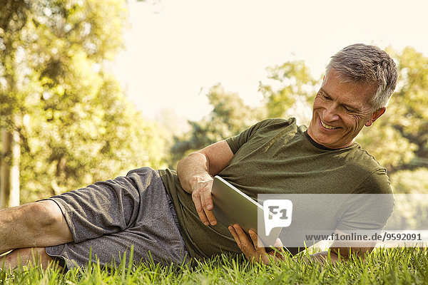 Der reife Mann sieht sich das digitale Tablett im Park an.