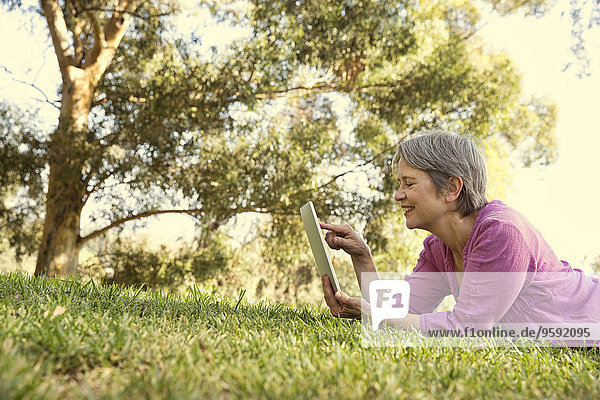 Reife Frau mit Touchscreen auf digitalem Tablett im Park