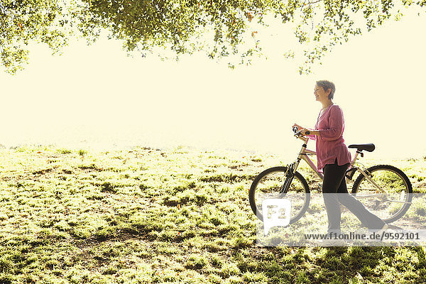 Reife Frau schiebt Fahrrad im Park