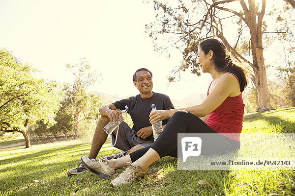 Mature running couple taking a break and drinking water in park