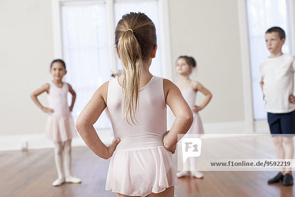 Four children practicing ballet with hands on hips in ballet school