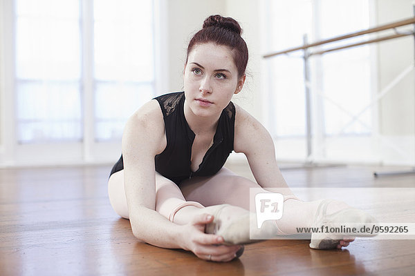 Teenager-Ballerina sitzend auf dem Boden in Ballettstellung in der Ballettschule