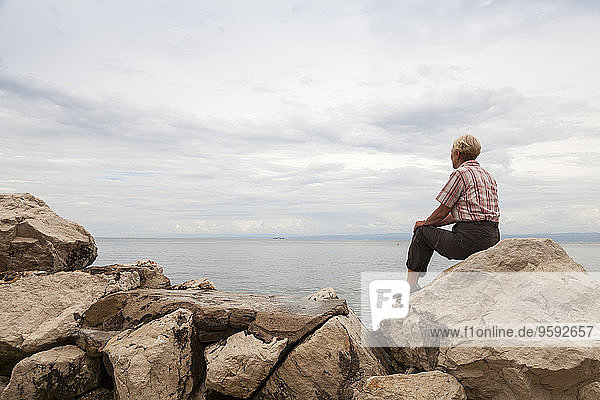 Slowenien  Piran  Frau auf Felsen am Wasser sitzend mit Blick auf den Horizont